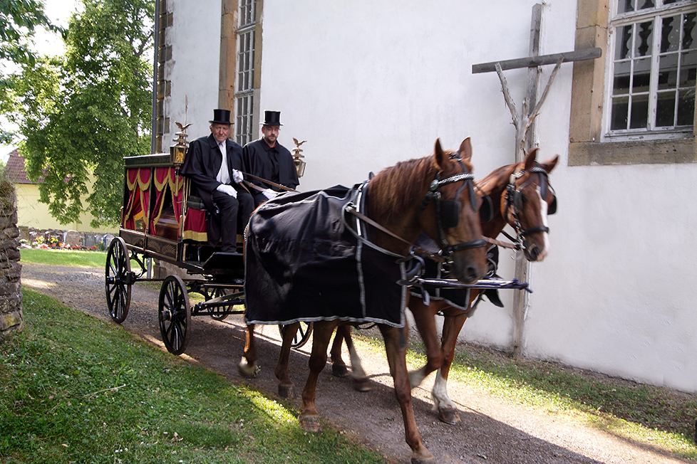 Wir informieren Sie gerne über die Art der Beisetzung Trauerkutsche fährt an der Kirche entlang